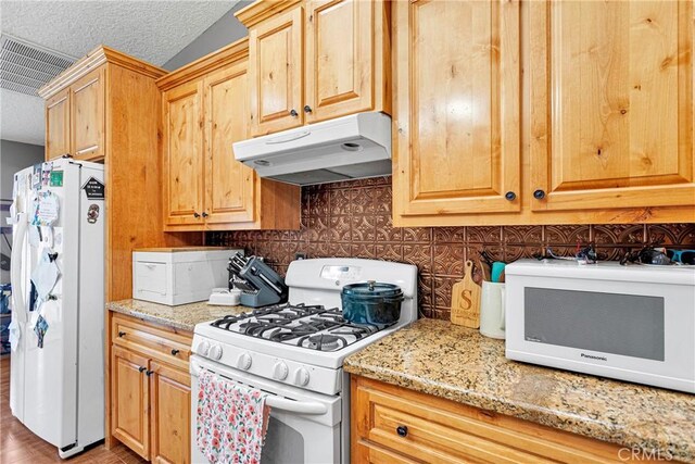 kitchen with tasteful backsplash, light stone counters, white appliances, and a textured ceiling