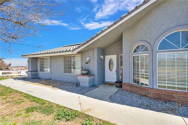 doorway to property featuring a tiled roof, fence, and stucco siding