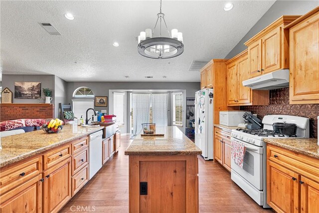 kitchen with decorative light fixtures, a center island, sink, white appliances, and a textured ceiling