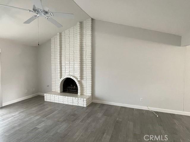 unfurnished living room featuring vaulted ceiling, ceiling fan, dark hardwood / wood-style flooring, and a brick fireplace