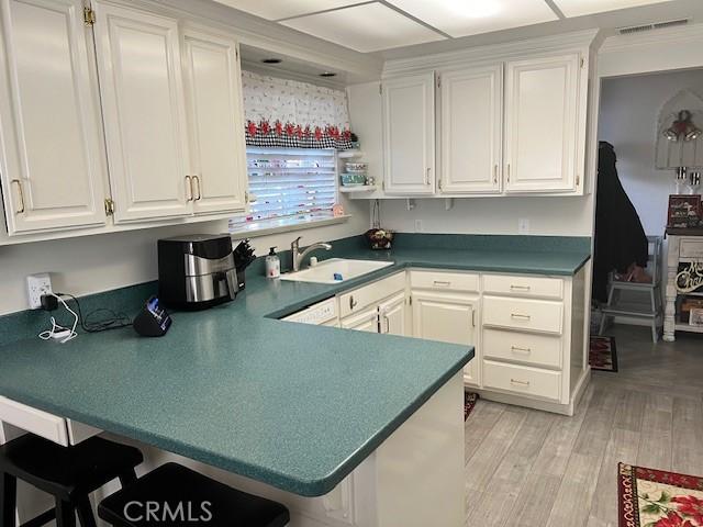 kitchen with kitchen peninsula, sink, white cabinetry, and light hardwood / wood-style floors