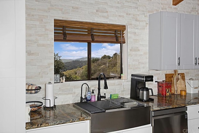 kitchen featuring white cabinetry, sink, dark stone countertops, backsplash, and stainless steel dishwasher