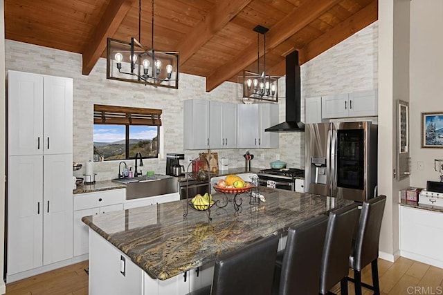 kitchen featuring white cabinets, a notable chandelier, sink, and wall chimney range hood