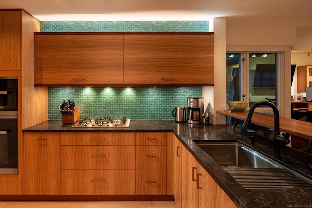 kitchen featuring tasteful backsplash, oven, sink, stainless steel gas cooktop, and dark stone counters