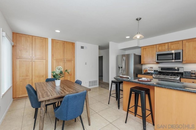 kitchen featuring dark stone counters, light tile patterned floors, a kitchen breakfast bar, pendant lighting, and stainless steel appliances