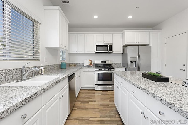 kitchen with white cabinetry, appliances with stainless steel finishes, light stone countertops, light hardwood / wood-style flooring, and sink