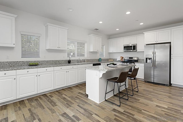 kitchen with light stone countertops, appliances with stainless steel finishes, a kitchen island, white cabinetry, and a breakfast bar area