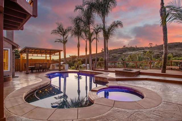 pool at dusk with an in ground hot tub, a mountain view, and a patio