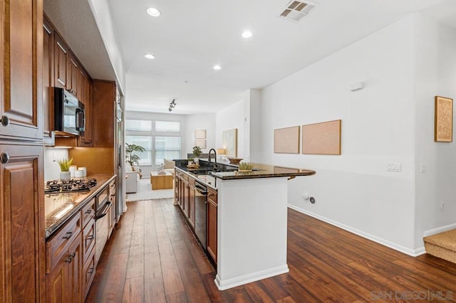 kitchen with an island with sink, appliances with stainless steel finishes, dark hardwood / wood-style floors, dark stone countertops, and sink