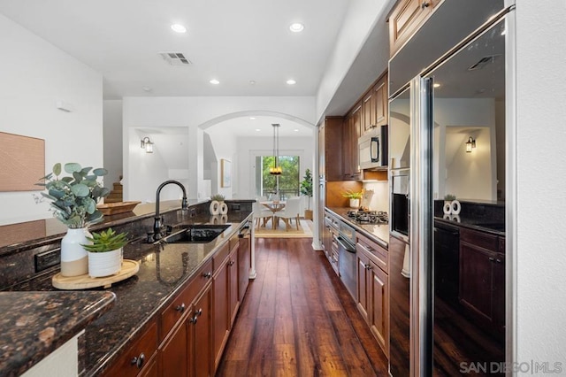 kitchen featuring dark hardwood / wood-style floors, dark stone countertops, sink, hanging light fixtures, and appliances with stainless steel finishes