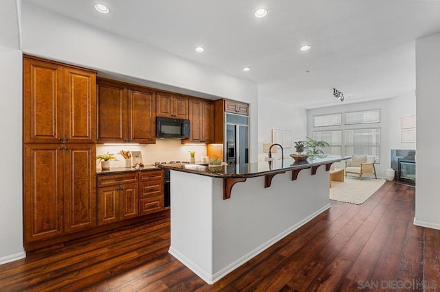 kitchen with a kitchen bar, dark hardwood / wood-style floors, stainless steel built in fridge, a kitchen island with sink, and a premium fireplace