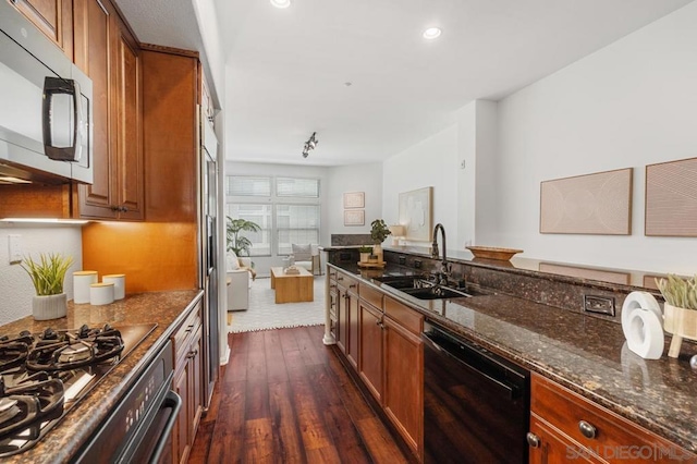 kitchen with appliances with stainless steel finishes, sink, dark hardwood / wood-style flooring, and dark stone counters