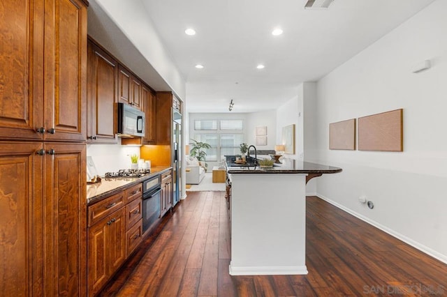 kitchen with a center island with sink, stainless steel gas cooktop, a breakfast bar area, dark hardwood / wood-style flooring, and black oven