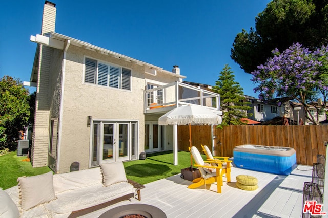 rear view of house featuring a hot tub, a fire pit, a yard, french doors, and a balcony