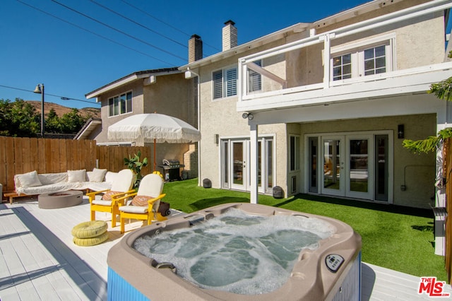 rear view of house featuring a deck, a hot tub, french doors, an outdoor living space with a fire pit, and a yard