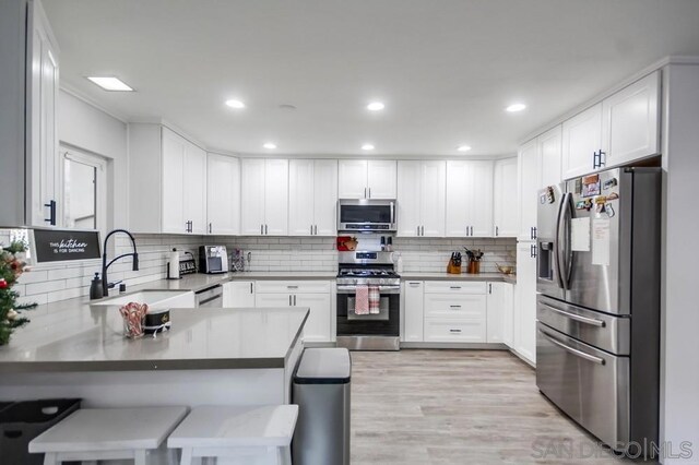 kitchen with a kitchen bar, kitchen peninsula, stainless steel appliances, and white cabinetry