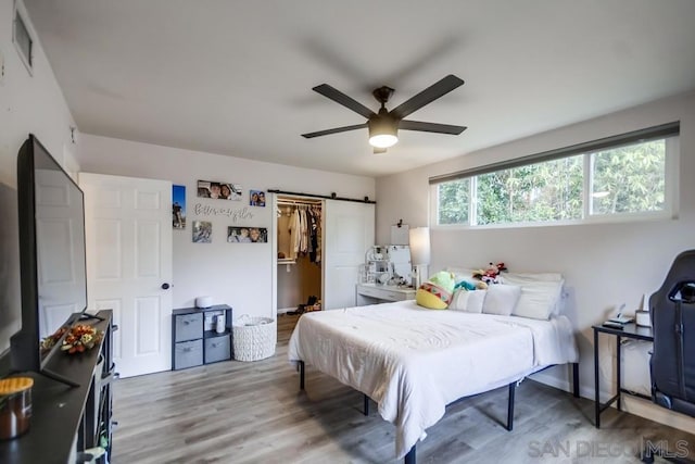 bedroom with ceiling fan, a barn door, hardwood / wood-style floors, a walk in closet, and a closet