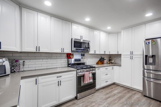 kitchen with white cabinets, light hardwood / wood-style flooring, stainless steel appliances, and tasteful backsplash