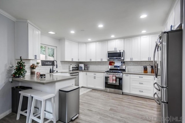 kitchen with kitchen peninsula, sink, white cabinetry, appliances with stainless steel finishes, and a breakfast bar area