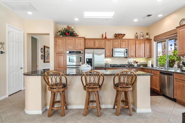 kitchen featuring light tile patterned floors, a skylight, appliances with stainless steel finishes, dark stone counters, and a kitchen island