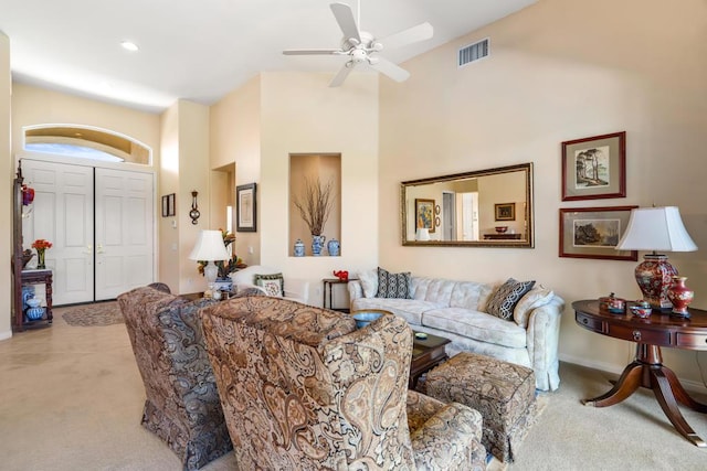 carpeted living room featuring ceiling fan and a towering ceiling