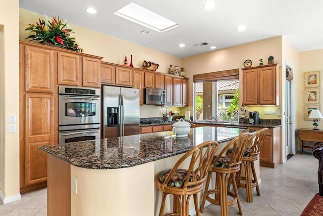 kitchen with a center island, stainless steel appliances, dark stone counters, and light tile patterned flooring