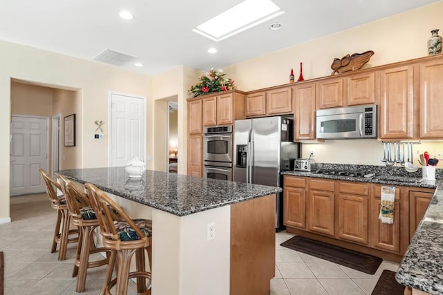 kitchen with dark stone countertops, a center island, a kitchen bar, stainless steel appliances, and light tile patterned floors