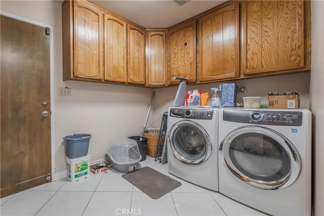 clothes washing area featuring cabinets, light tile patterned floors, and washing machine and clothes dryer