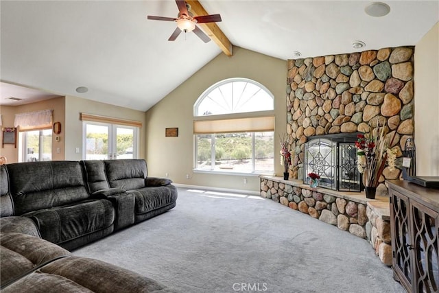 carpeted living room with ceiling fan, lofted ceiling with beams, and a stone fireplace