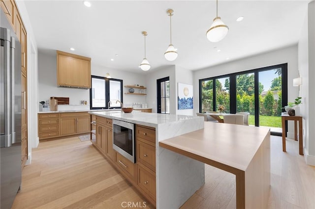 kitchen with decorative light fixtures, a kitchen island, light hardwood / wood-style flooring, appliances with stainless steel finishes, and light stone counters