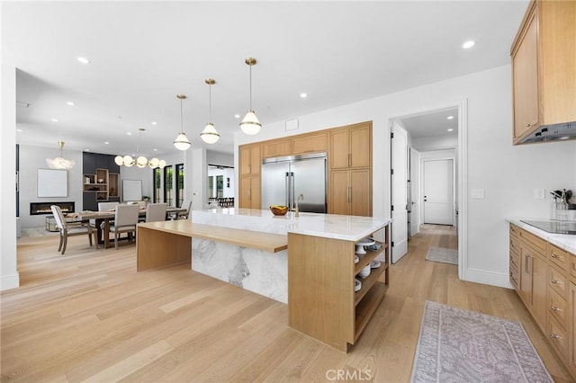 kitchen with built in refrigerator, decorative light fixtures, an island with sink, and light hardwood / wood-style flooring