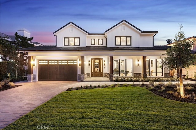 modern farmhouse style home featuring a garage, a porch, and a lawn