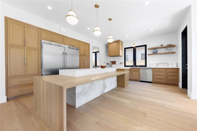 kitchen with light hardwood / wood-style floors, appliances with stainless steel finishes, decorative light fixtures, a kitchen island, and sink