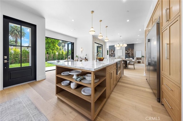 kitchen with a large island with sink, built in appliances, light hardwood / wood-style flooring, hanging light fixtures, and light stone counters