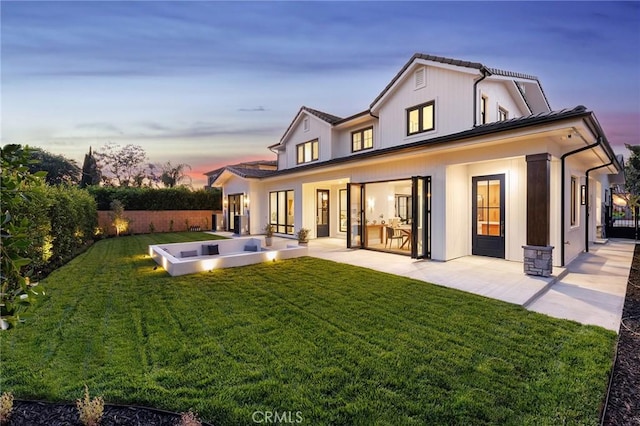 back house at dusk featuring a lawn and a patio