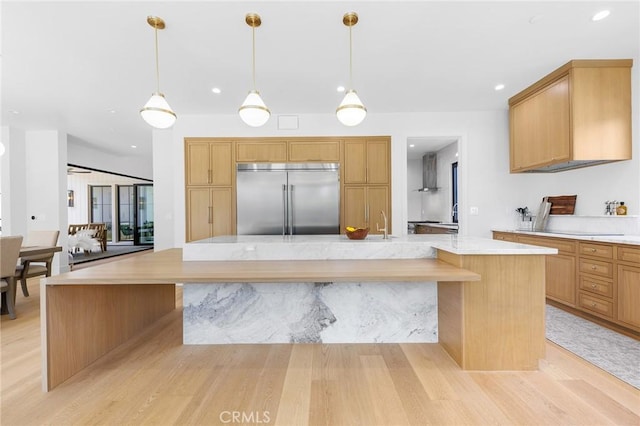 kitchen featuring pendant lighting, sink, light wood-type flooring, stainless steel built in fridge, and a large island