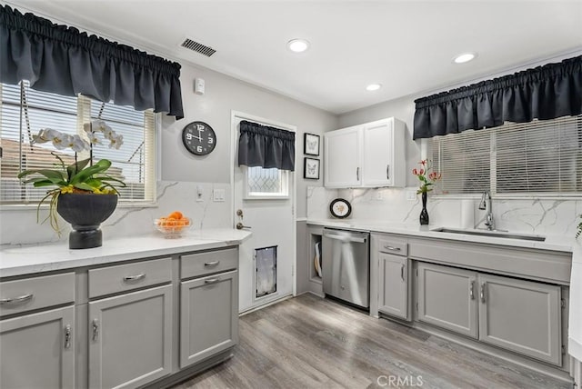 kitchen with stainless steel dishwasher, decorative backsplash, sink, and gray cabinetry