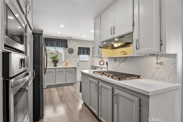 kitchen with backsplash, gray cabinets, stainless steel appliances, and light wood-type flooring