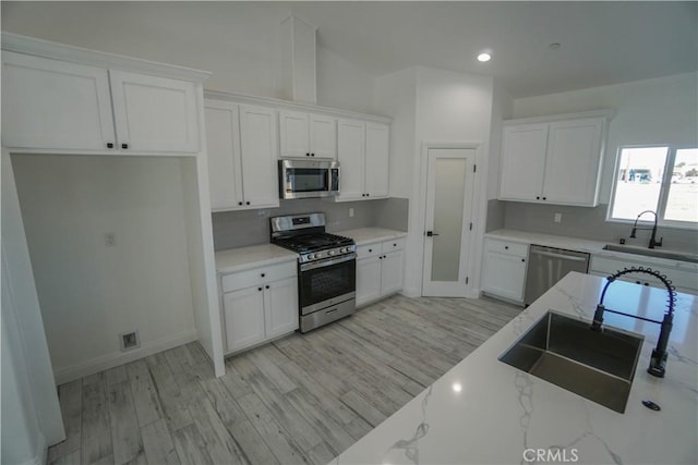 kitchen with white cabinets, light stone countertops, sink, and stainless steel appliances