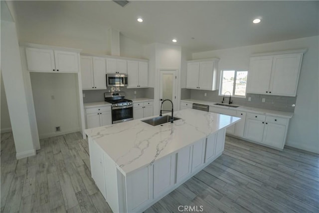 kitchen with sink, white cabinetry, a kitchen island with sink, stainless steel appliances, and light stone counters