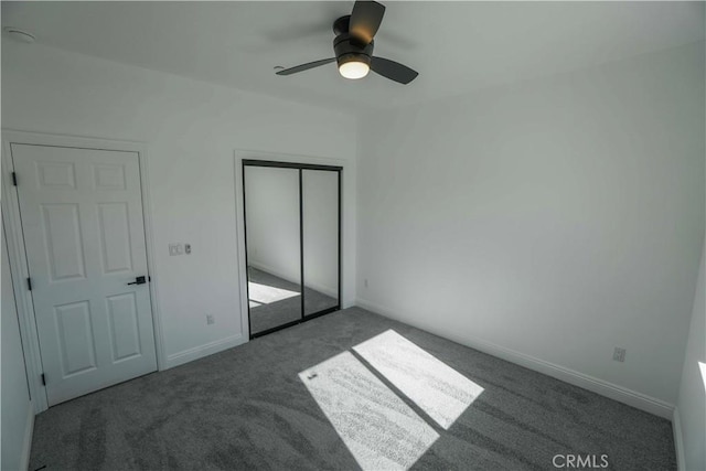 unfurnished bedroom with ceiling fan, a closet, and dark colored carpet