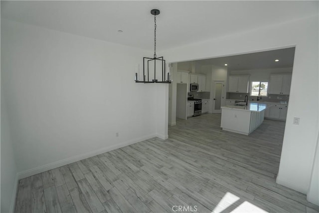 unfurnished dining area with an inviting chandelier, light hardwood / wood-style flooring, and sink