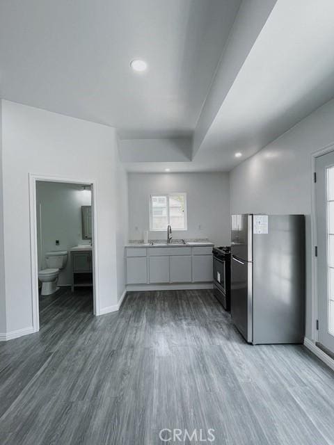 kitchen with gas stove, hardwood / wood-style floors, sink, white cabinetry, and stainless steel fridge