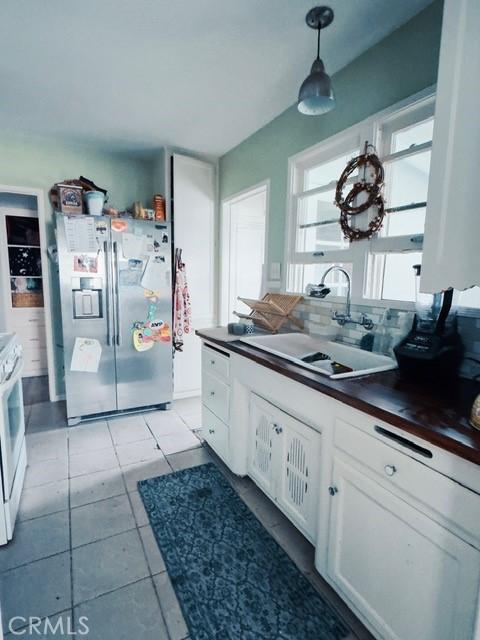 kitchen featuring decorative light fixtures, sink, white range, white cabinets, and stainless steel fridge