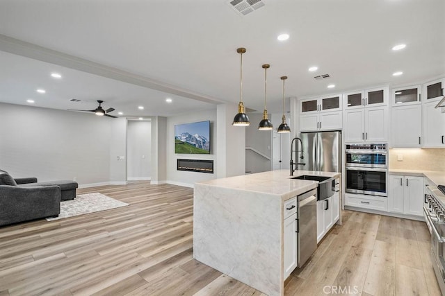 kitchen with appliances with stainless steel finishes, white cabinetry, sink, hanging light fixtures, and a center island with sink