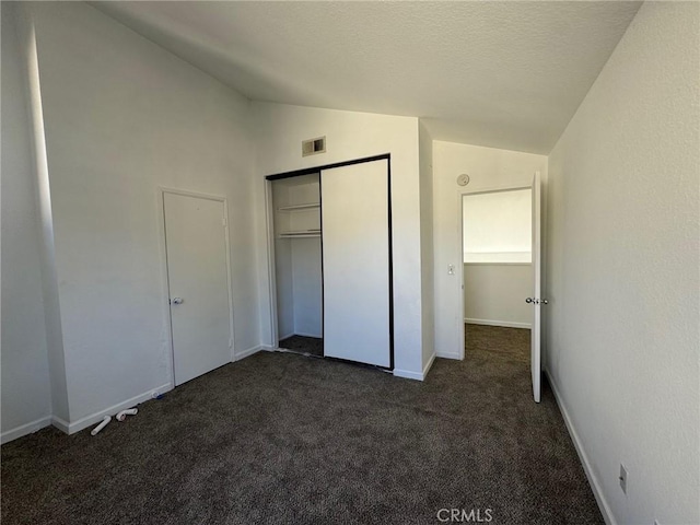 unfurnished bedroom featuring a closet, lofted ceiling, and dark colored carpet