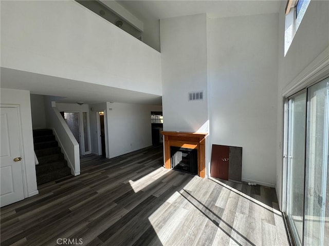 unfurnished living room featuring a healthy amount of sunlight, a towering ceiling, and dark hardwood / wood-style floors