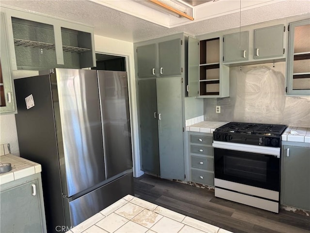 kitchen featuring decorative backsplash, stainless steel fridge, tile countertops, and gas stove