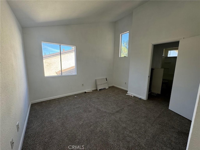 unfurnished room featuring lofted ceiling and dark carpet