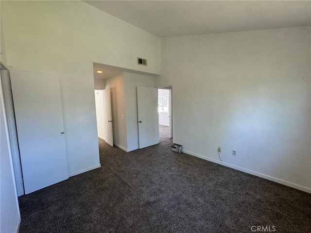 unfurnished bedroom featuring a towering ceiling and dark colored carpet